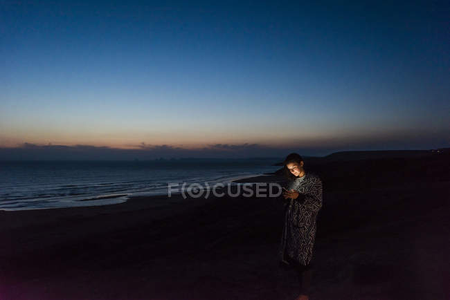 Jovem mulher usando smartphone na praia no crepúsculo — Fotografia de Stock