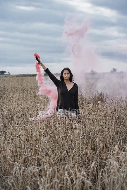 Retrato de jovem em pé no campo de milho com tocha de fumaça — Fotografia de Stock