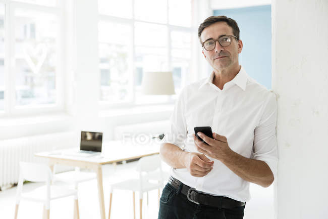 Empresário com telefone celular em pé no escritório brilhante — Fotografia de Stock