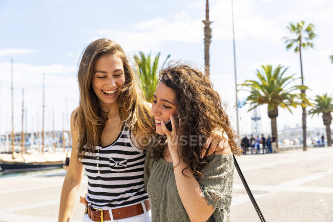Zwei glückliche Freundinnen mit Handy an der Uferpromenade — Stockfoto