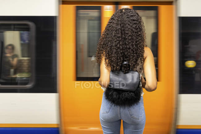 Vista trasera de la joven mujer esperando en la plataforma de la estación de metro - foto de stock
