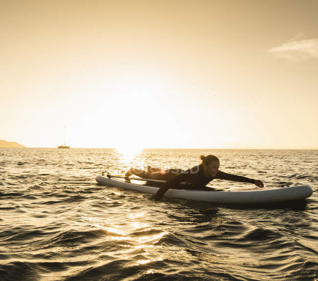 Giovane donna sdraiata sul paddleboard al tramonto — Foto stock