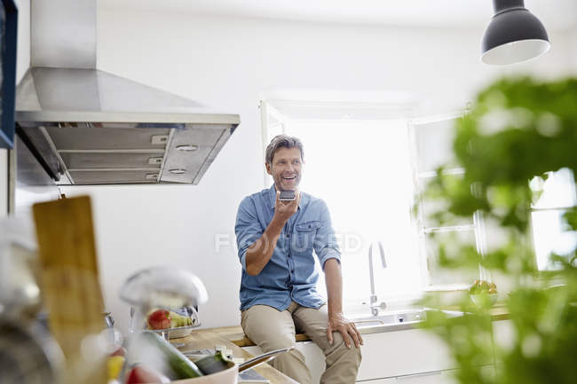 Homem maduro na cozinha falando no smartphone — Fotografia de Stock