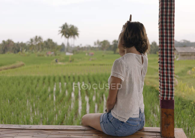 Молодая женщина сидит на скамейке и смотрит на рисовое поле — стоковое фото