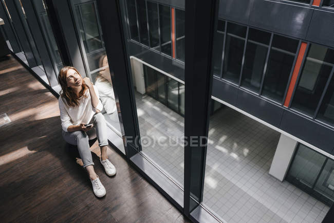 Businesswoman with smartphone, sitting on floor and daydreaming — Stock Photo