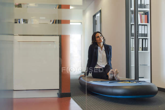 Barefoot Businesswoman sitting on sup paddle board, daydreaming in ...