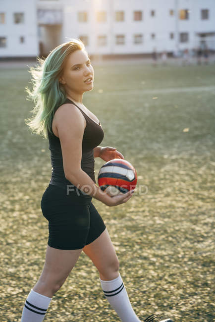 Молодая женщина ходит по футбольному полю, держа мяч — стоковое фото