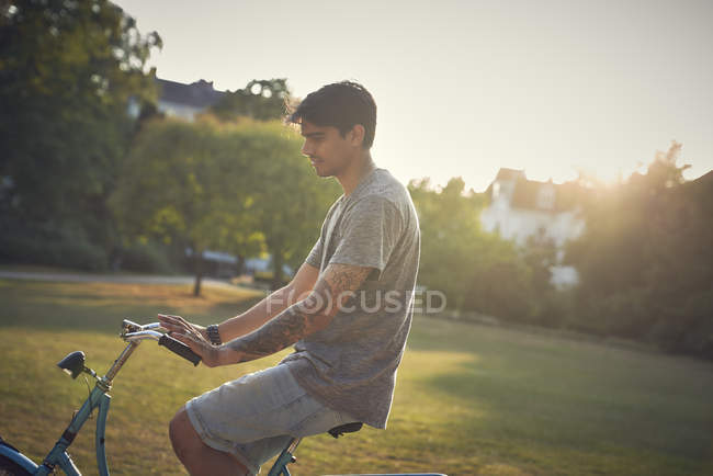 Giovane uomo in bicicletta in parco al tramonto — Foto stock