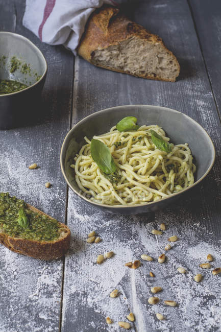 Homemade basil pesto, spaghetti in a bowl, rye baguette on wood — Stock Photo