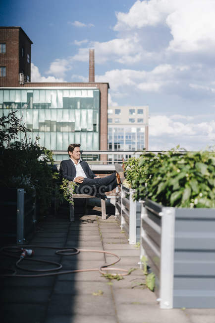 Businessman relaxing in urban rooftop garden — Stock Photo