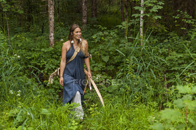 Улыбающаяся женщина, идущая по лесу с луком и стрелами — стоковое фото
