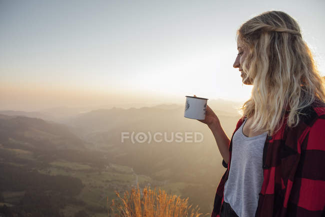 Suiza, Grosser Mythen, joven en un viaje de senderismo al amanecer sosteniendo una taza - foto de stock