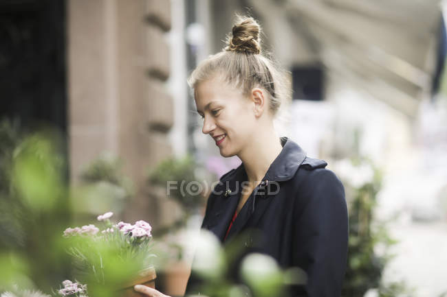 Smiling young woman choosing potted plant in front of a flower shop — Stock Photo
