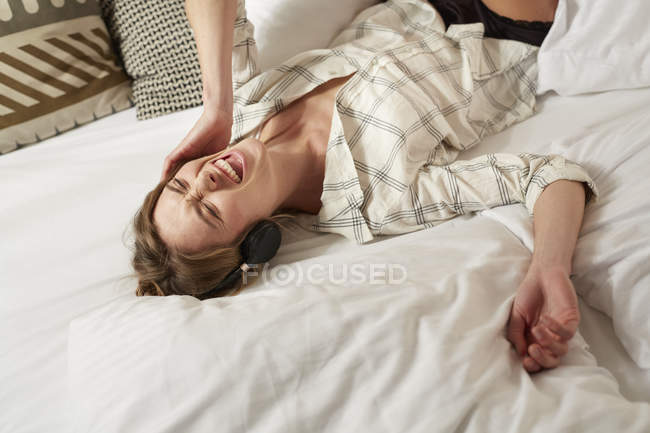Portrait of laughing woman lying on bed with headphones — Stock Photo