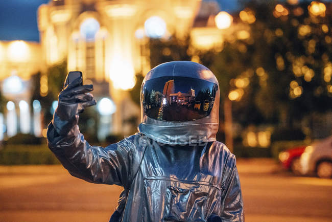Spaceman in city at night taking a selfie with smartphone — Stock Photo