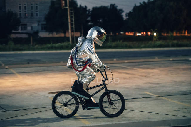 Spaceman en la ciudad por la noche en el estacionamiento montando bicicleta bmx - foto de stock