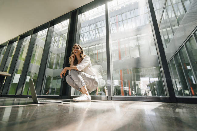 Happy businesswoman crouching on floor in modern office — Stock Photo