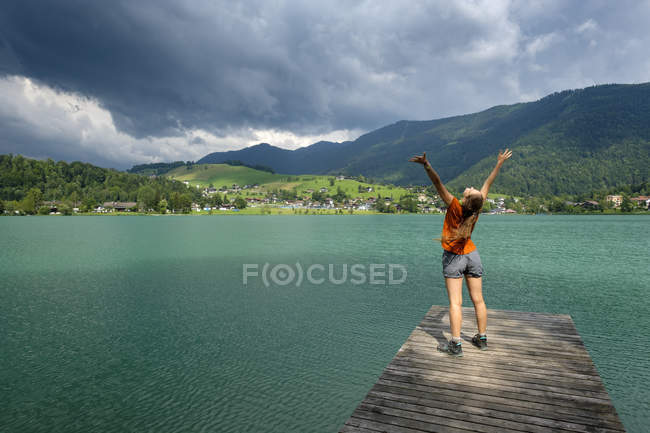 Adolescente em pé no molhe de madeira, braços levantados — Fotografia de Stock