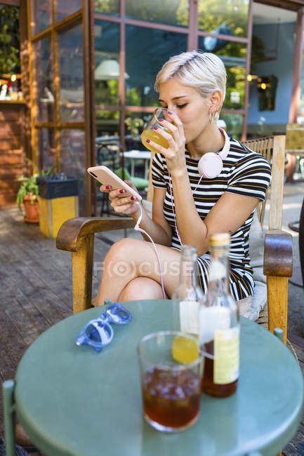 Молода жінка в кафе покриття покриття насолоджується безалкогольним напоєм, дивлячись на смартфон. — стокове фото