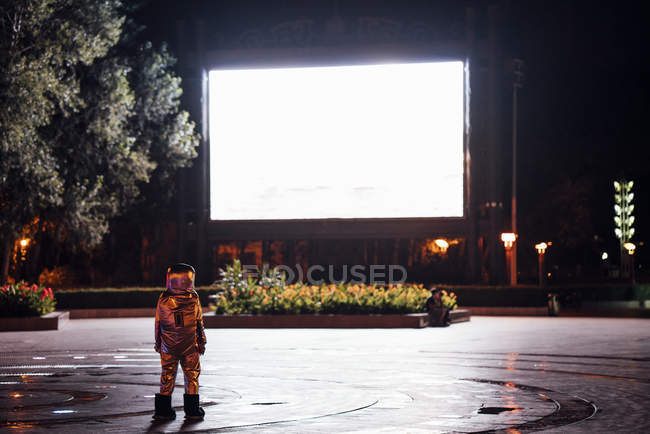 Spaceman standing on square at night attracted by shining projection screen — Stock Photo