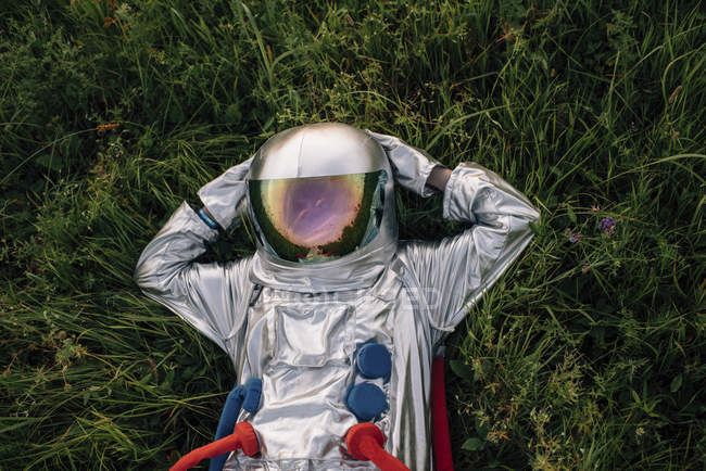 Astronauta relajándose en el prado verde con las manos detrás de la cabeza - foto de stock
