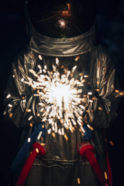 Spaceman de pie al aire libre en la noche y la celebración de sparkler - foto de stock