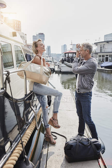 Uomo più anziano scattare foto di giovane donna sul molo accanto allo yacht — Foto stock