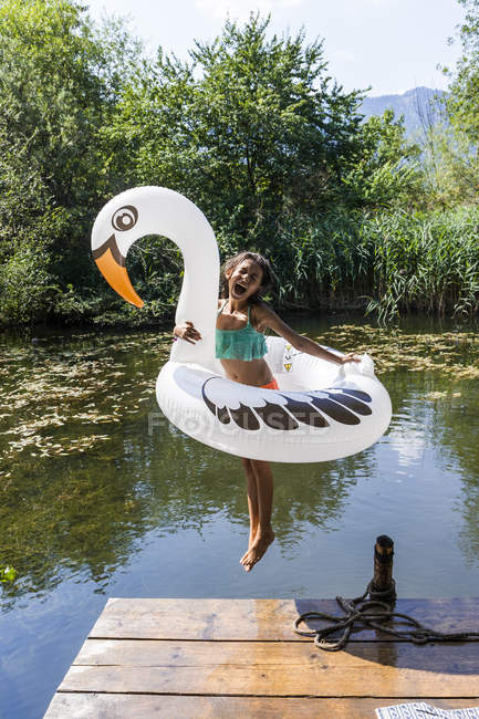Carefree girl jumping into pond with inflatable pool toy in swan shape — Stock Photo