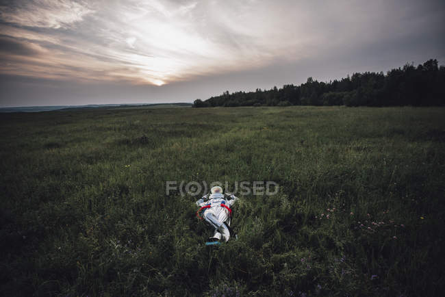 Spaceman relaxing in green meadow under cloudy sky — Stock Photo