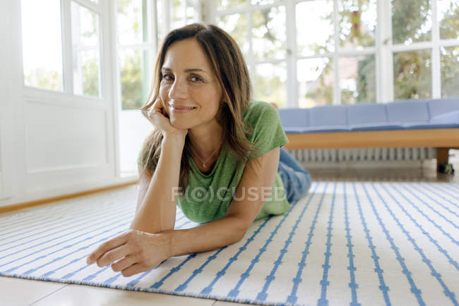 Портрет посміхаючись зрілої жінки лежачи на підлозі в будинку — стокове фото