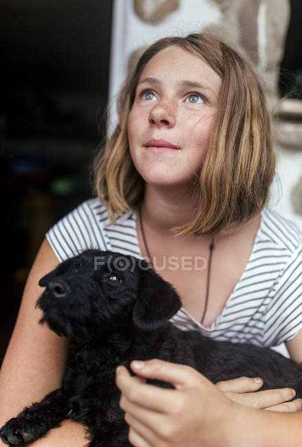 Portrait of freckled girl with black puppy in her arms looking up — Stock Photo