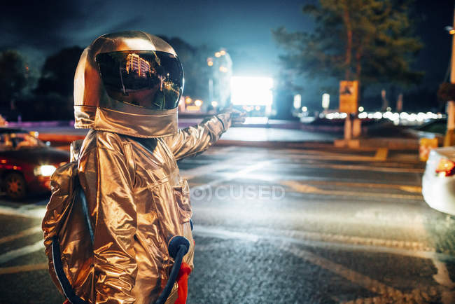 Космонавт на улице в городе ночью указывает на сияющий проекционный экран — стоковое фото