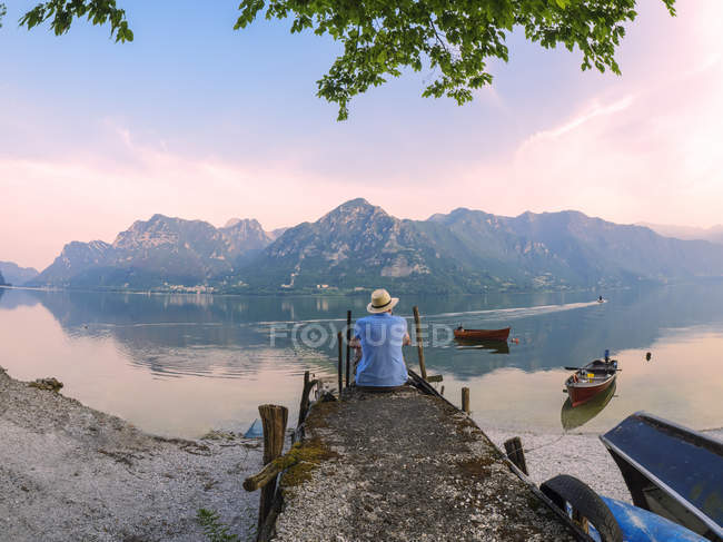 Італія, Ломбардія, вигляд людини сидить на пристані на озері Ідро під час ранкових сутінок. — стокове фото