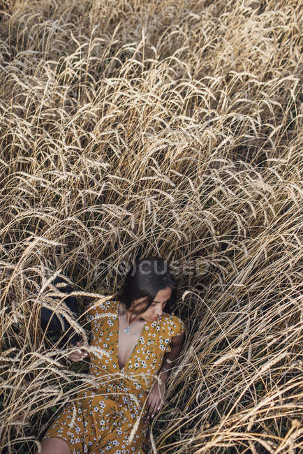 Giovane donna che indossa abito estivo con disegno floreale sdraiato nel campo di mais — Foto stock