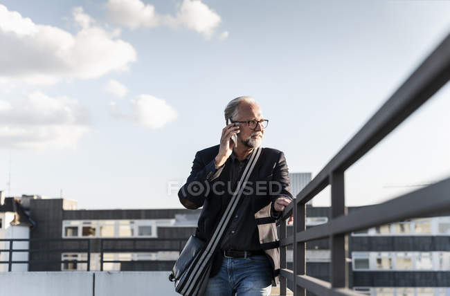 Reifer Mann steht auf Dach, stützt sich auf Geländer, benutzt Smartphone — Stockfoto