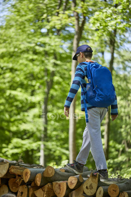 Хлопчик з рюкзаком балансує на колодах у лісі. — стокове фото
