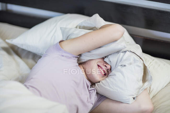 Menino deitado na cama segurando travesseiro sobre a cabeça — Fotografia de Stock