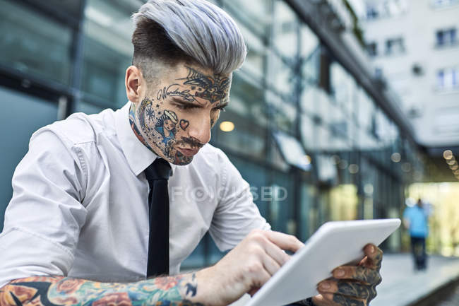 Молодой бизнесмен с татуированным лицом, с помощью цифрового планшета — стоковое фото