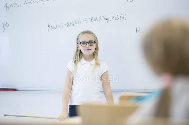 Шкільна дівчинка стоїть на дошці з формулою в класі. — стокове фото