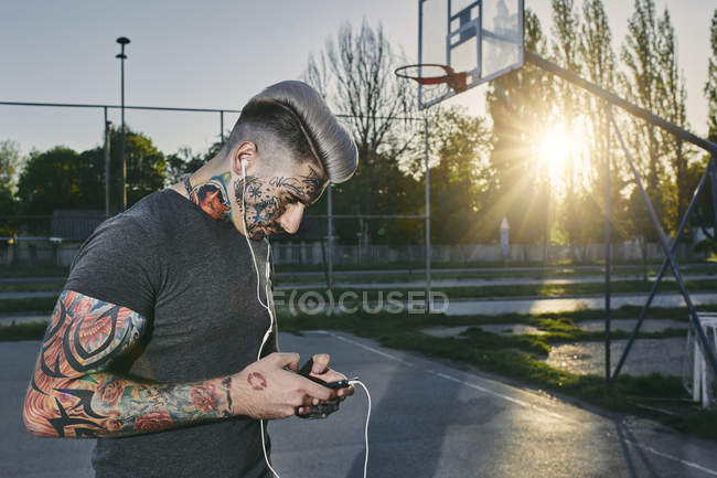 Татуированный молодой человек со смартфоном и наушниками — стоковое фото