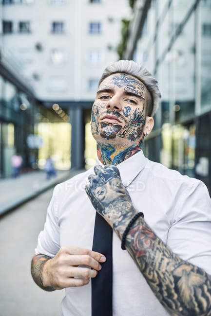 Молодой бизнесмен с татуированным лицом, застегивающий галстук — стоковое фото
