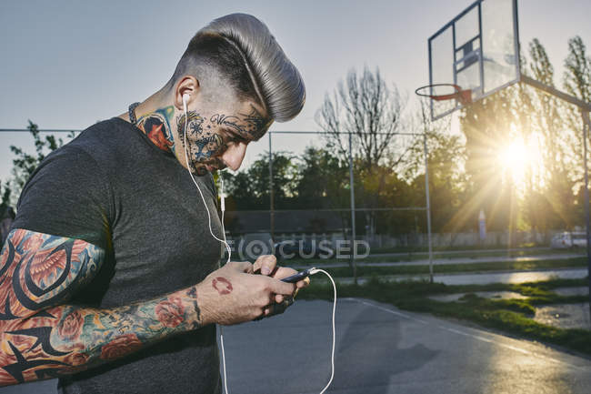 Tatuato giovane uomo con smartphone e auricolari — Foto stock