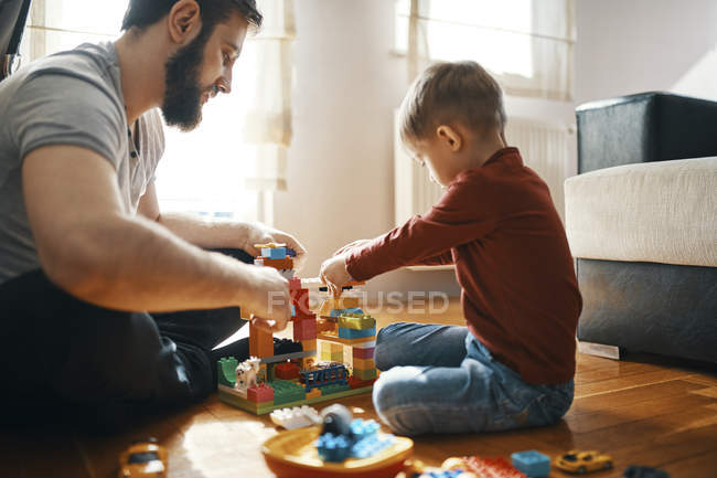 Father and son sitting on the floor  playing together with building bricks — Stock Photo