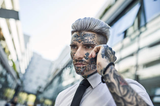 Молодий бізнесмен з татуюванням обличчям, говорячи по телефону — стокове фото