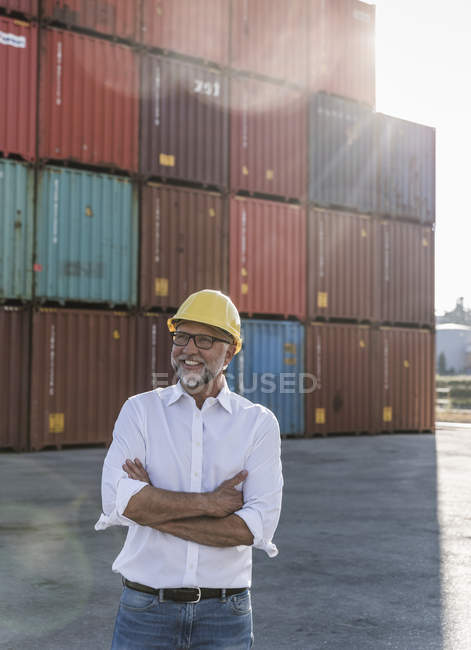 Businessman at cargo harbour, wearing safety helmet, arms crossed — Stock Photo