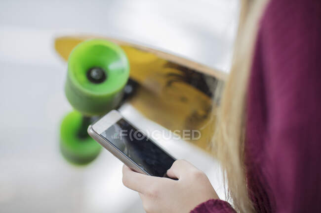 Крупный план девочки-подростка, держащей скейтборд и мобильный телефон — стоковое фото