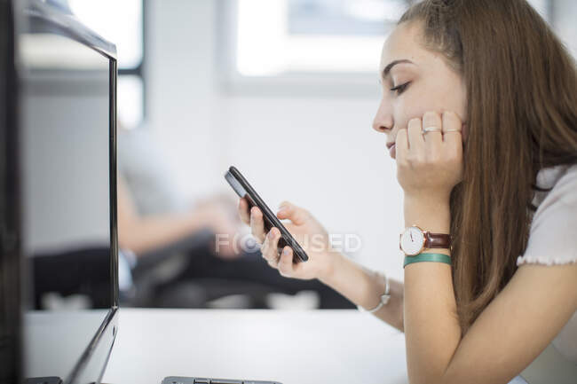 Adolescente utilizando el teléfono celular en la clase de informática - foto de stock