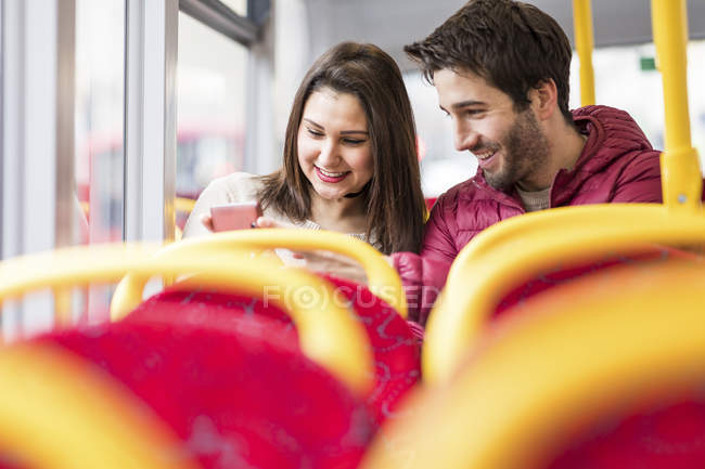 UK, London, happy young couple in bus looking at cell phone — Stock Photo