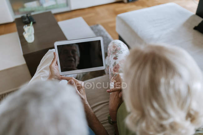 Casal de idosos em casa sentado no sofá compartilhando tablet — Fotografia de Stock
