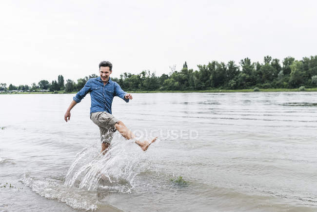 Lachender Mann, der Wasser in einen Fluss spritzt — Stockfoto